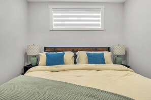 Un dormitorio con cama, dos mesitas de noche, una ventana con persianas y una lámpara de pared.