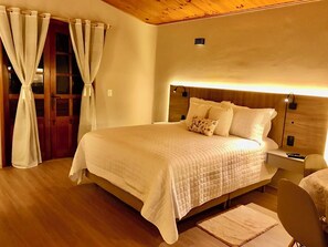 Une chambre d’hôtel avec un plafond en bois, un lit recouvert d’une courtepointe matelassée, une table de chevet avec une lampe et une chaise.