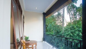 Un balcón con mesa y sillas de madera, una planta pequeña en maceta y vistas a exuberante vegetación.