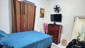 A bedroom with a bed, a ceiling fan, an air conditioning unit, a television, a dresser, and a door. - Luxury house in soothing Spanish Town perfect for your getaway (Spanish Town)
