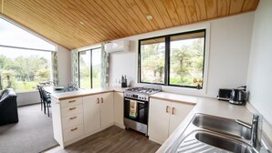 A modern kitchen with wooden ceiling, large windows, and a view of greenery.