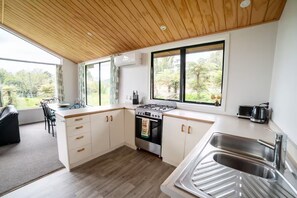 Cocina moderna con techo de madera, ventanas amplias y vista a zonas verdes.