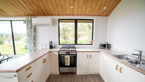 A modern kitchen with white cabinets, a wooden ceiling, and a large window overlooking a garden.