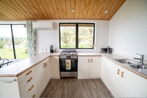 Una cocina moderna con armarios blancos, techo de madera y un ventanal con vistas a un jardín.