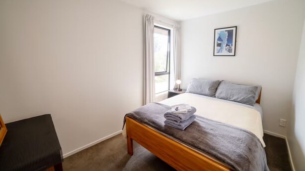 A bedroom with a bed, a nightstand, a chair, a window with curtains, and a framed picture on the wall.