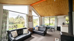 A cozy living room with a fireplace, leather sofas, a dining table, and large windows offering a view of the outdoors.