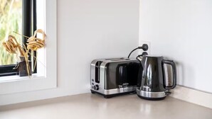 Eine Küchenarbeitsplatte mit einem Toaster und einem Wasserkocher, ein Fenster mit getrockneten Blumen und eine weiße Wand.