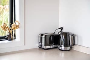 Eine Küchenarbeitsplatte mit einem Toaster und einem Wasserkocher, ein Fenster mit getrockneten Blumen und eine weiße Wand.