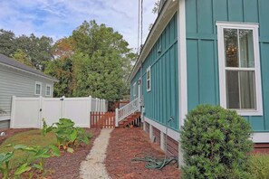 A house with a pathway leading to a wooden deck, surrounded by a white fence and a small garden.
