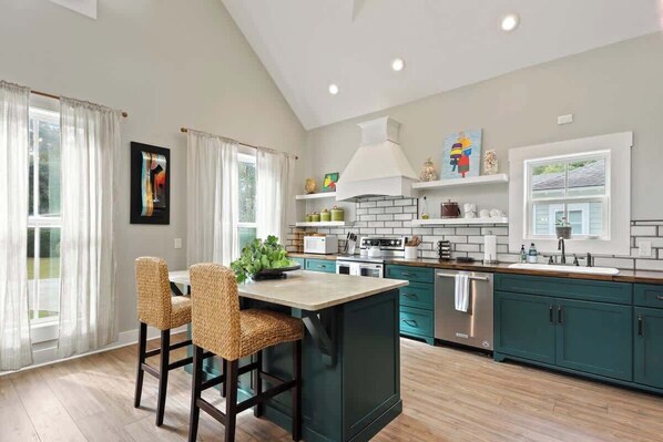 A modern kitchen with a central island, teal cabinetry, and a large window.