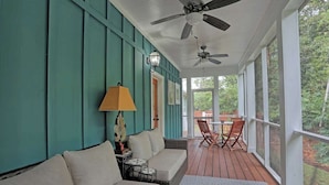 Eine überdachte Veranda mit Deckenventilator, einer Couch, einem Tisch, Stühlen und einer Lampe.