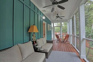 A covered porch with a ceiling fan, a sofa, a table, chairs, and a lamp.