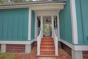 A covered porch with a wooden staircase leading to a door, surrounded by teal siding. - Sweet Cottage + Studio Near Wormsloe Historic Site (Savannah)