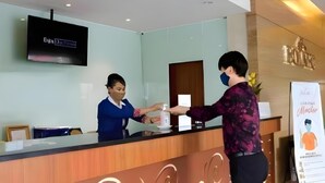A reception desk with a flat-screen TV mounted above it, a wooden counter, and a wall-mounted sign with text. - Borneo Hotel (Pontianak)