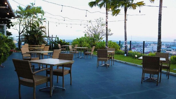 An outdoor seating area with tables and chairs, surrounded by greenery and overlooking a cityscape. - Borneo Hotel (Pontianak)