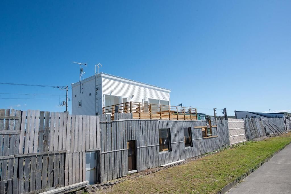 A modern building with a flat roof, a wooden deck, and a fenced area.