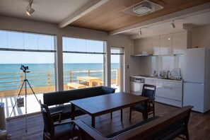 A modern kitchen with large windows overlooking the sea, a dining area with a bench, and a tripod with a camera.