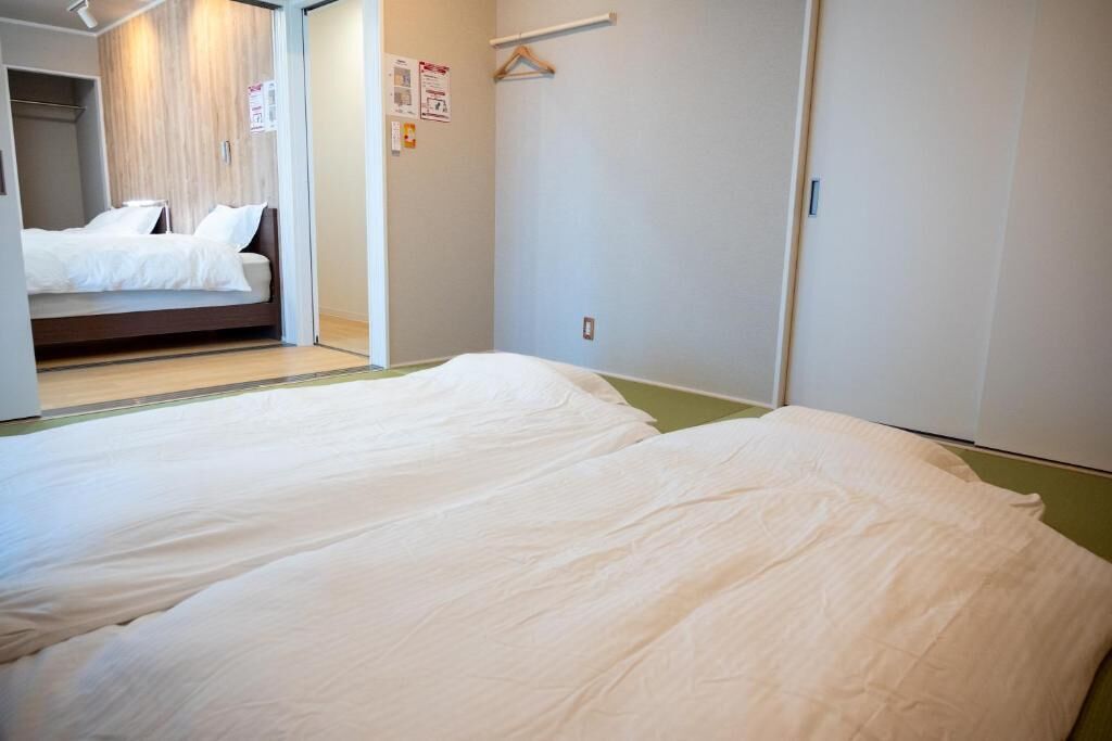 A hotel room with two beds, a wooden wardrobe, and a small seating area.