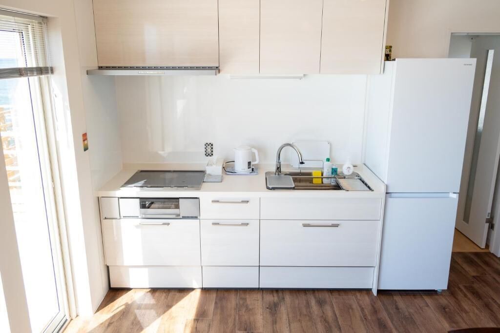 A compact kitchen with white cabinets, a built-in oven, a sink, and a refrigerator.