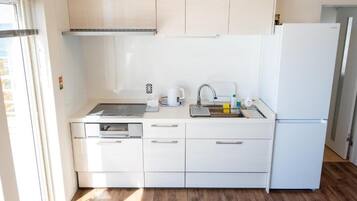 A compact kitchen with white cabinets, a built-in oven, a sink, and a refrigerator.