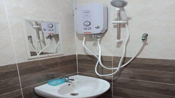 A bathroom with a white sink, a handheld showerhead, and a wall-mounted control panel. - SBR Inn (Semporna)