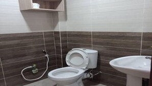 A bathroom with a toilet, a sink, and a wooden shelf above the toilet. - SBR Inn (Semporna)