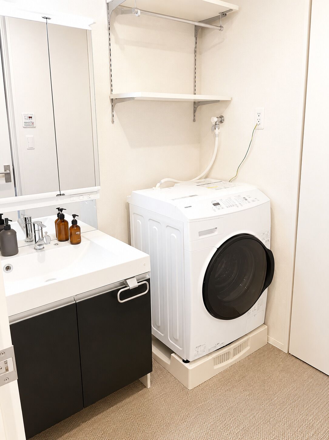 A compact bathroom with a white sink, mirror, and a front-loading washing machine.