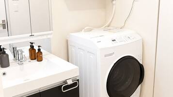 A compact bathroom with a white sink, mirror, and a front-loading washing machine.