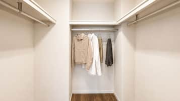 A walk-in closet with a wooden floor, white walls, and a hanging rod with clothes.