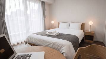 A hotel room with a bed, bedside lamps, a laptop on a desk, and a chair.