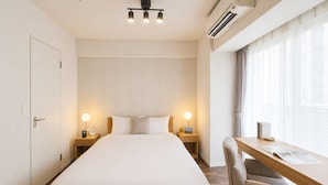 Ett hotellrum med en säng, sänglampor, ett skrivbord med en stol och en luftkonditioneringsanläggning.
