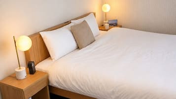 A neatly made bed with white bedding, two bedside lamps, and a wooden nightstand with a small shelf.