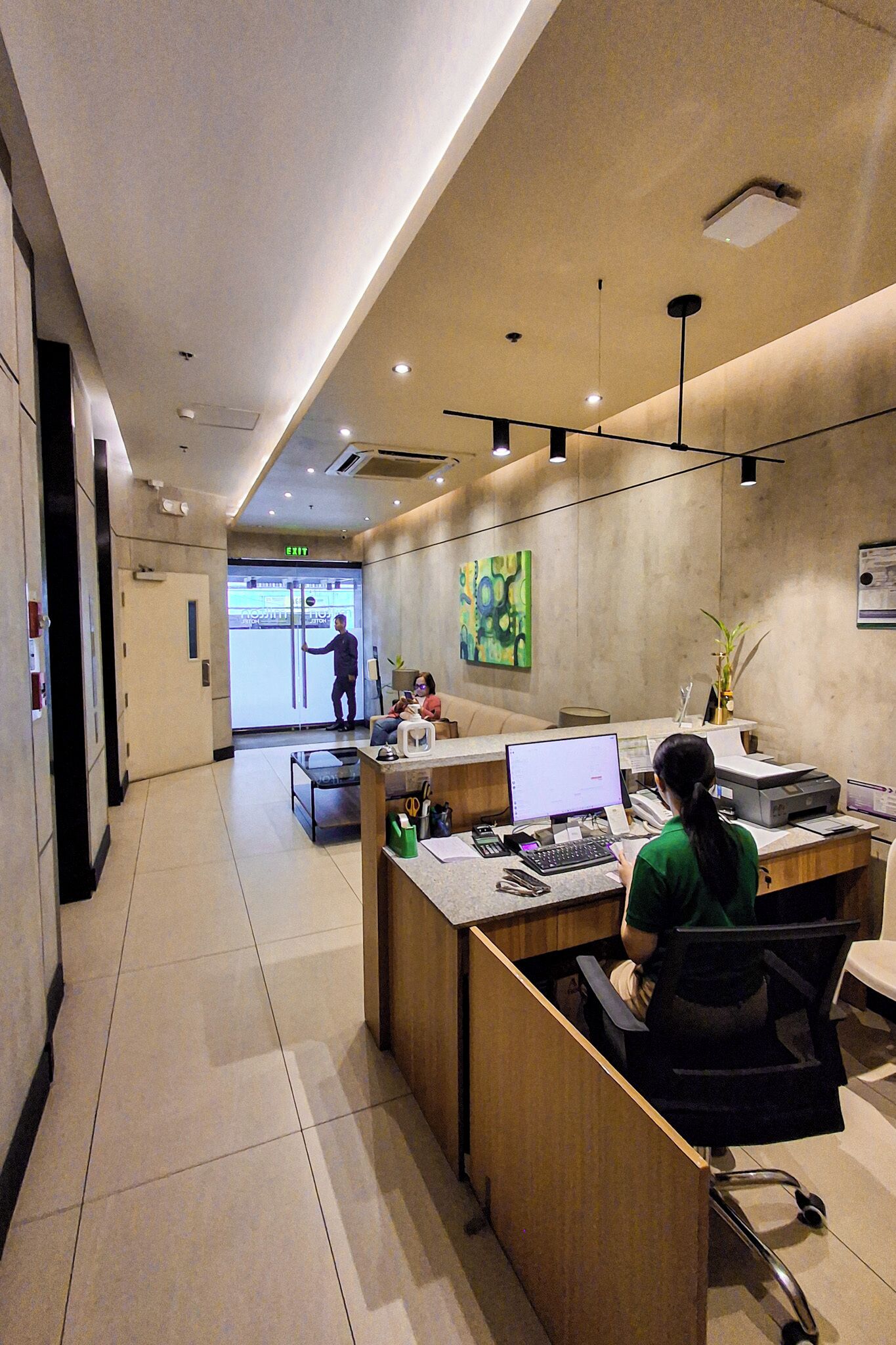 Zona de recepción de un hotel con escritorio, computadora y una persona sentada.