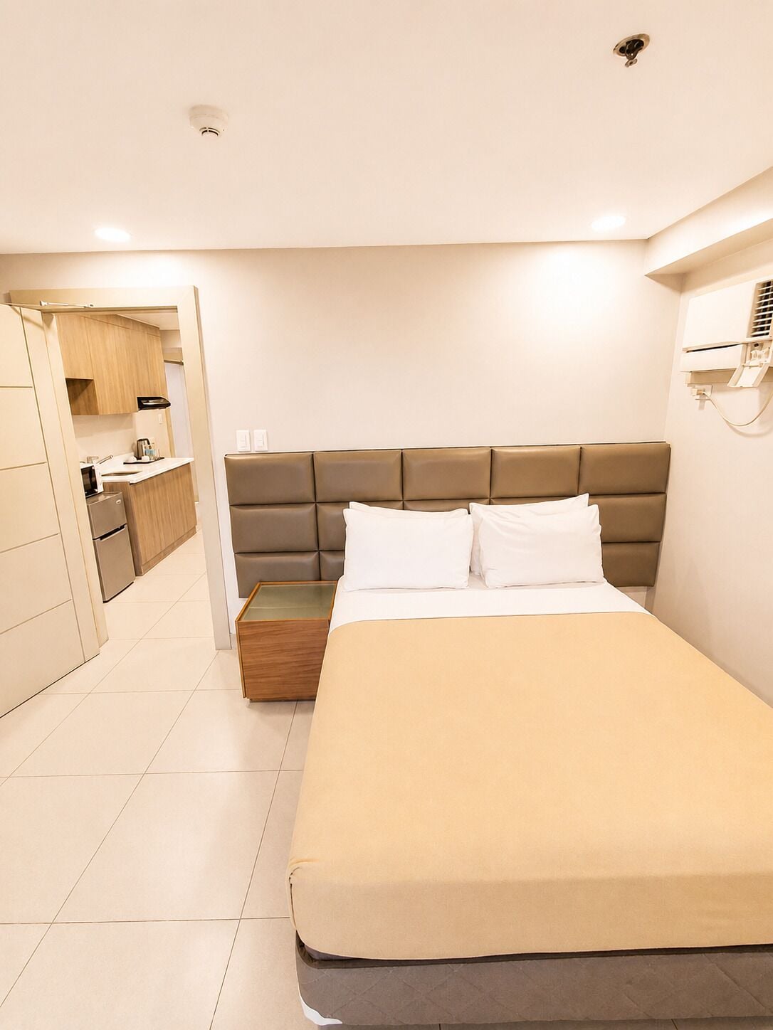 A bedroom with a bed, a bedside table, a wardrobe, and a kitchenette area.