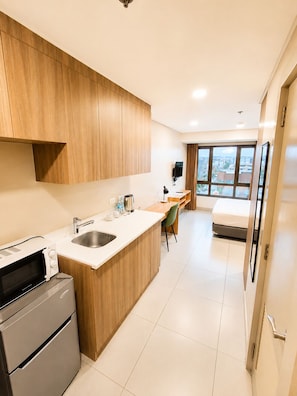 Habitación de hotel compacta con kitchenette, una cama, un escritorio y vistas a la ciudad a través de amplios ventanales.