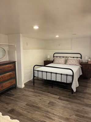A bedroom with a bed, dresser, bedside tables, and a window.