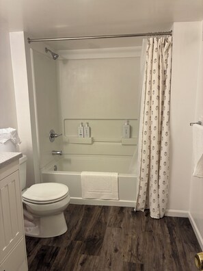 Et badeværelse med toilet, badekar, bruser og toiletpapirholder.