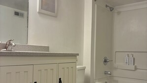 Un baño con tocador blanco, inodoro, zona de ducha y espejo con luces.