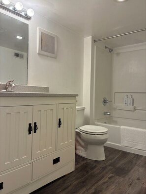 Un baño con tocador blanco, inodoro, zona de ducha y espejo con luces.