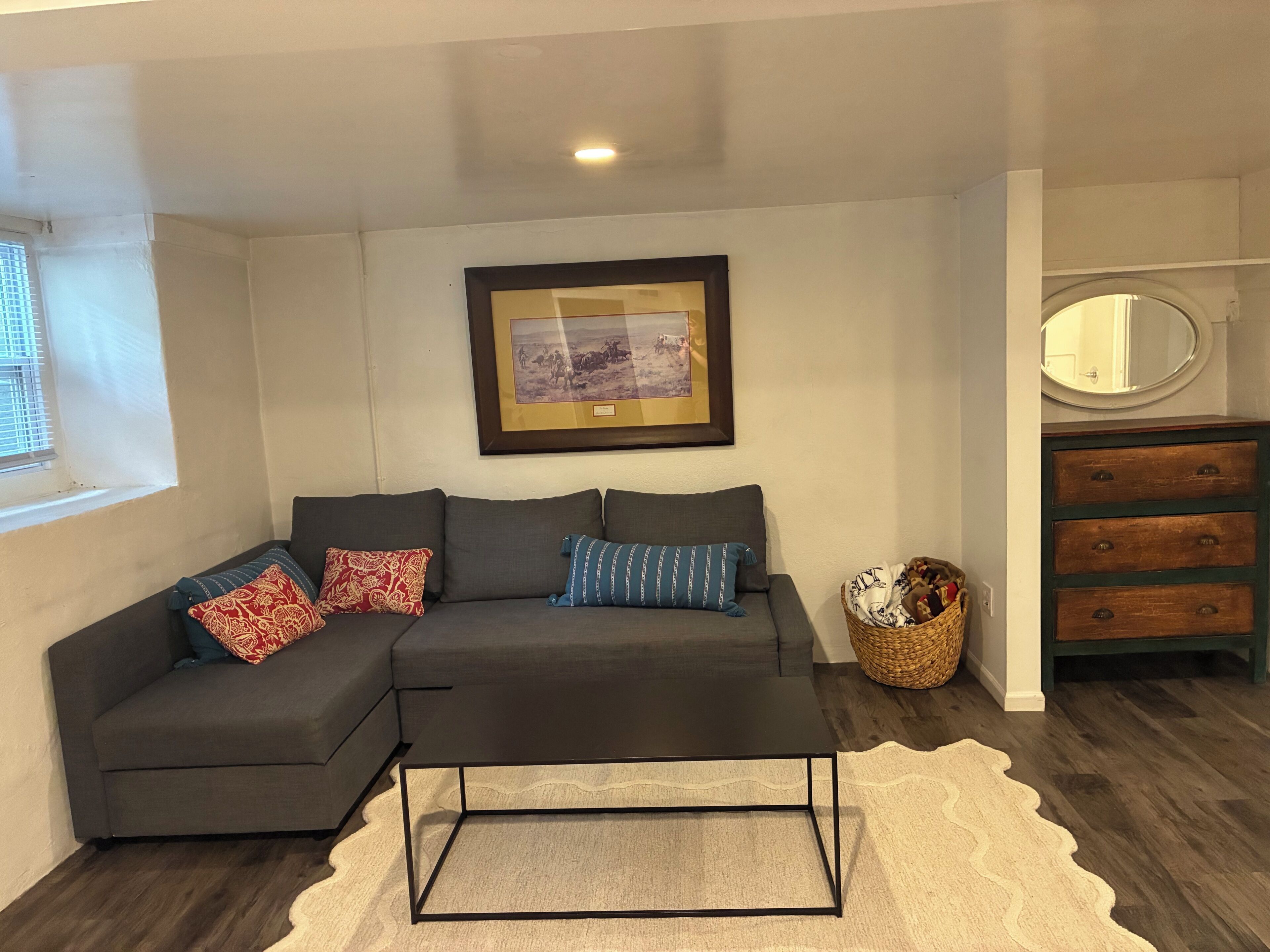 A modern living room with a sectional sofa, a coffee table, a framed picture on the wall, a mirror, and a wooden dresser.