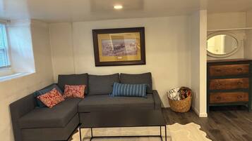 A modern living room with a sectional sofa, a coffee table, a framed picture on the wall, a mirror, and a wooden dresser.