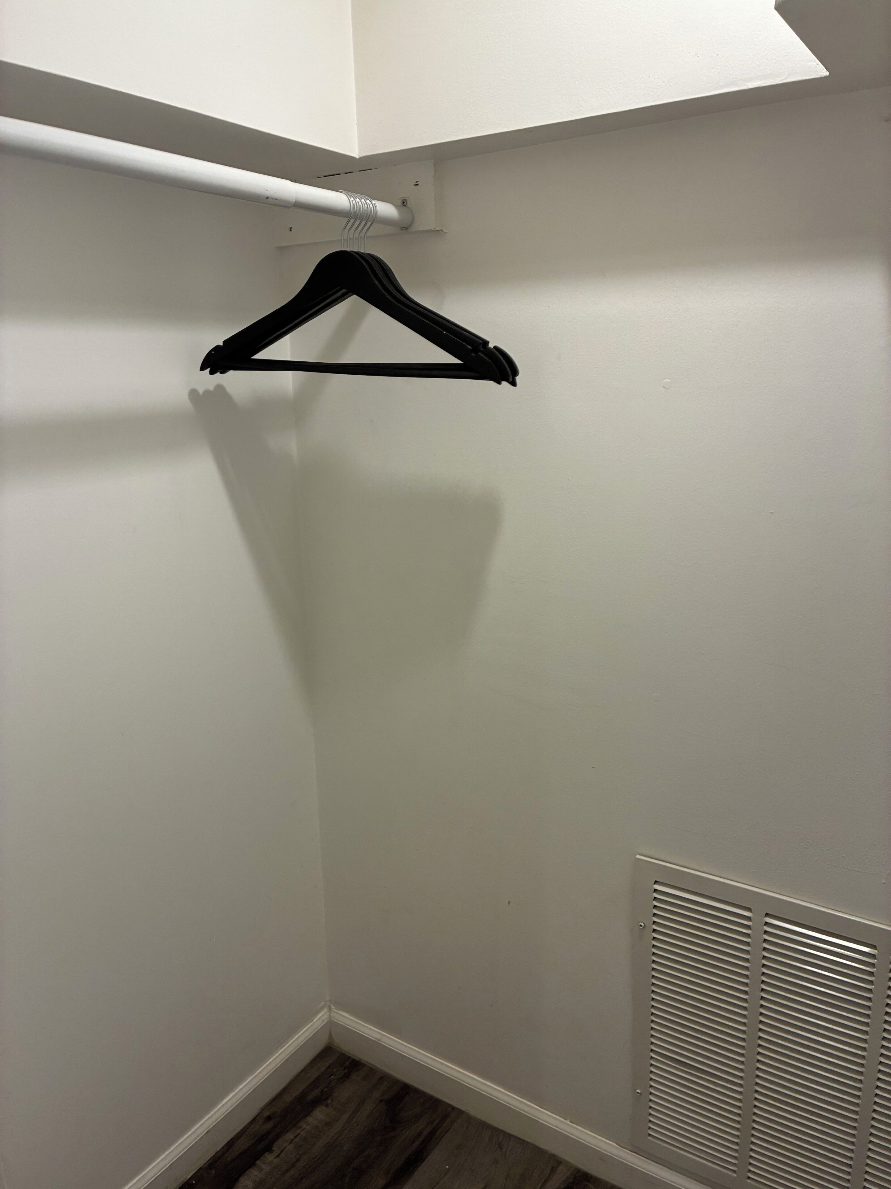 A closet with a white wall, a wooden floor, and a white vent.