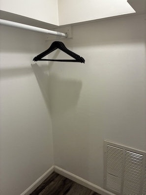 Un armario con pared blanca, piso de madera y rejilla blanca.