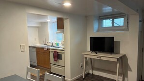 Una cocina compacta con un lavamanos, estufa y un televisor sobre una mesita.
