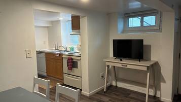 A compact kitchen with a sink, stove, and a TV on a small table.