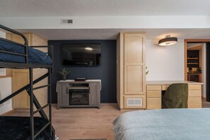 Ein Stockbett, ein Schreibtisch mit Stuhl, ein Fernseher, eine Kommode und eine kleine Pflanze.