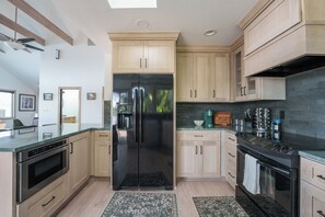 Eine moderne Küche mit hellen Holzschränken, einem schwarzen Kühlschrank, Edelstahlgeräten und einer dunklen Spritzschutzwand.