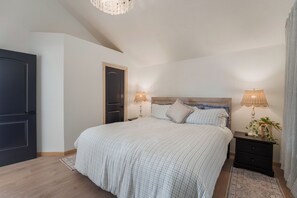 A bedroom with a large bed, two bedside tables with lamps, a dark door, and a wooden headboard.