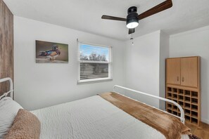 A bedroom with a bed, a ceiling fan, a window with blinds, a wooden cabinet, and a wall-mounted picture of a bird. - Golden Splash, HotTub & Fire Pit, 15 Min2CVG (Florence)