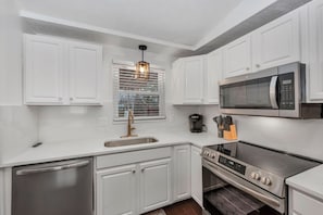 A modern kitchen with white cabinets, stainless steel appliances, a built-in oven, and a window with blinds. - Golden Splash, HotTub & Fire Pit, 15 Min2CVG (Florence)